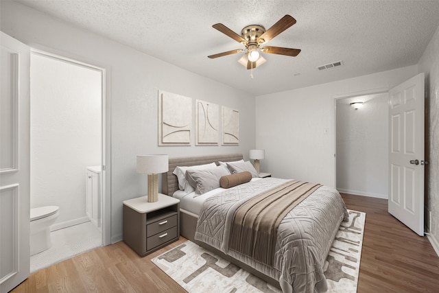 bedroom with a textured ceiling, light wood-type flooring, ensuite bathroom, and ceiling fan