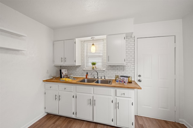 kitchen with white cabinets, decorative backsplash, light wood-type flooring, and sink