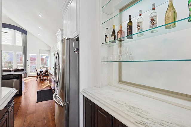 bar with stainless steel appliances, vaulted ceiling, light stone countertops, and dark brown cabinetry