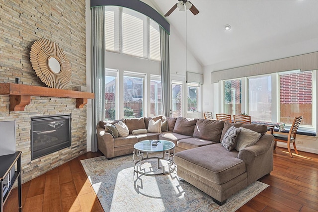 living room featuring a stone fireplace, dark wood-type flooring, high vaulted ceiling, and ceiling fan