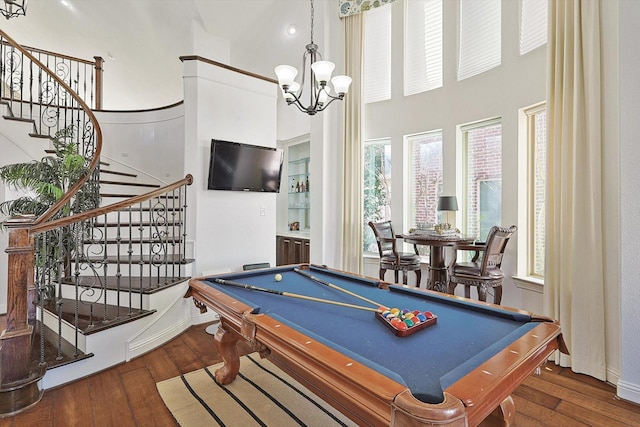 game room with an inviting chandelier, a towering ceiling, dark hardwood / wood-style flooring, and billiards