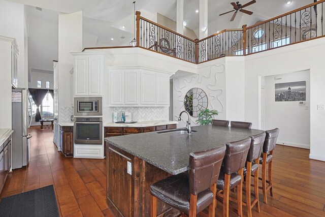 kitchen with an island with sink, backsplash, a breakfast bar area, dark brown cabinets, and sink