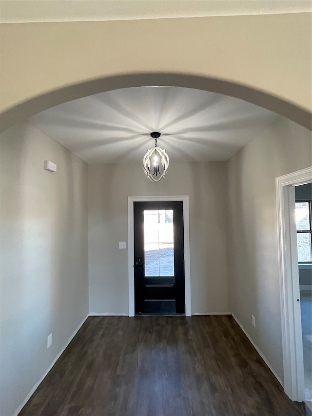 foyer entrance with an inviting chandelier, arched walkways, a wealth of natural light, and dark wood-type flooring