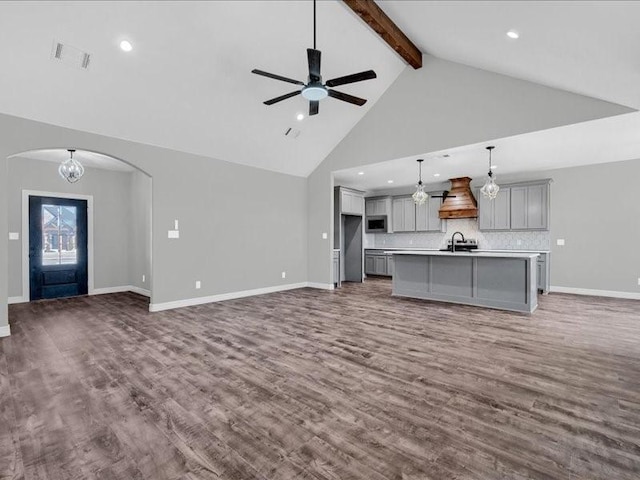 unfurnished living room with visible vents, beam ceiling, ceiling fan with notable chandelier, wood finished floors, and arched walkways