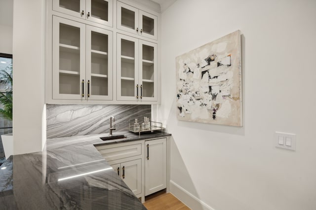 bar with dark stone counters, white cabinets, sink, light wood-type flooring, and tasteful backsplash