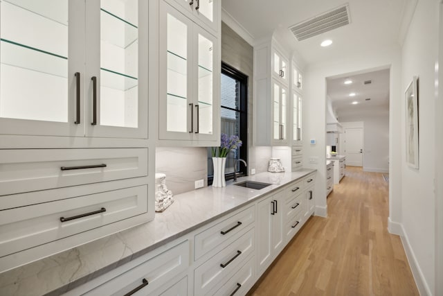 bar featuring light stone counters, crown molding, sink, white cabinets, and light hardwood / wood-style floors