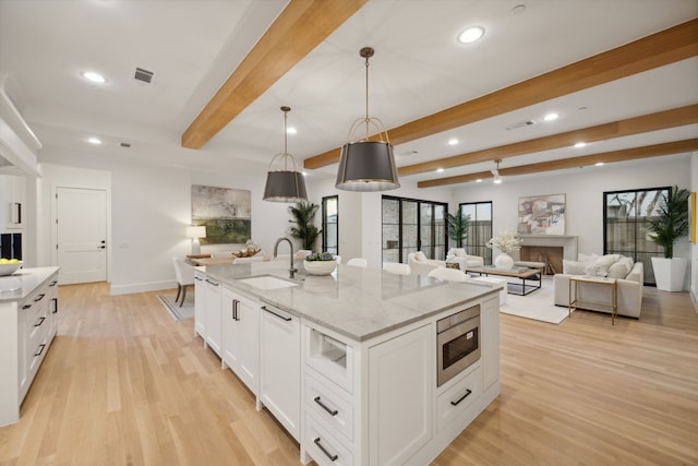 kitchen featuring a kitchen island with sink, sink, pendant lighting, beamed ceiling, and stainless steel microwave