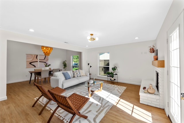 living room featuring a fireplace, a healthy amount of sunlight, light wood-type flooring, and an inviting chandelier