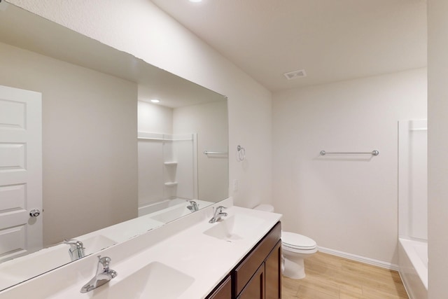 full bath with double vanity, toilet, a sink, wood finished floors, and baseboards