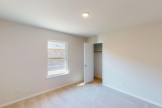 unfurnished bedroom with a closet, light colored carpet, and baseboards