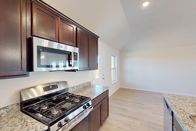 kitchen featuring lofted ceiling, light stone counters, stainless steel appliances, dark brown cabinets, and light wood-type flooring