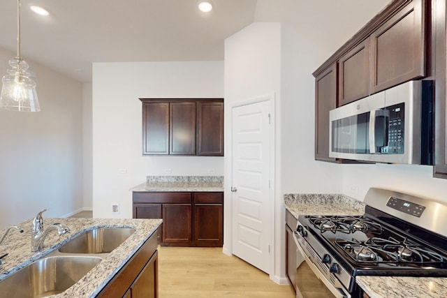 kitchen featuring light stone counters, stainless steel appliances, a sink, hanging light fixtures, and light wood-type flooring