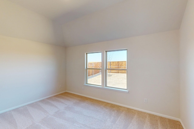 spare room featuring lofted ceiling, baseboards, and light colored carpet