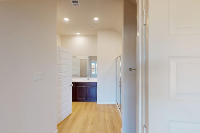 hall with light wood-style flooring, recessed lighting, a sink, visible vents, and baseboards