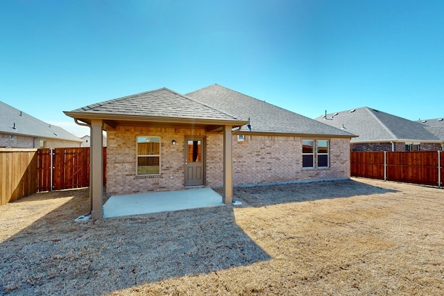 rear view of house featuring a shingled roof, a patio area, brick siding, and a fenced backyard