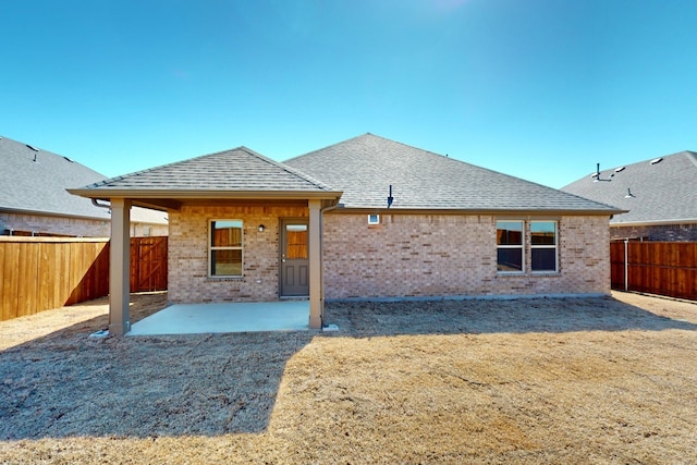 rear view of house with a patio area, brick siding, a fenced backyard, and roof with shingles