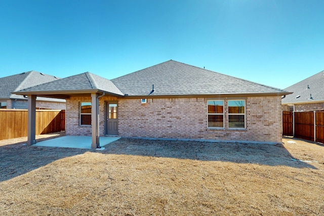 rear view of property featuring brick siding, a shingled roof, a fenced backyard, and a patio