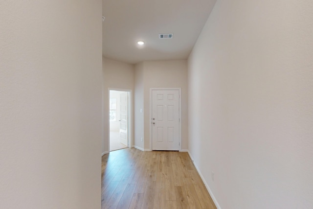 corridor with light wood-style flooring, visible vents, and baseboards