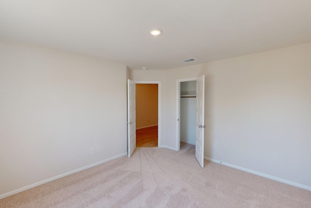 unfurnished bedroom with a closet, visible vents, light carpet, and baseboards