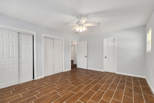 unfurnished bedroom with dark hardwood / wood-style flooring, ceiling fan, and multiple closets