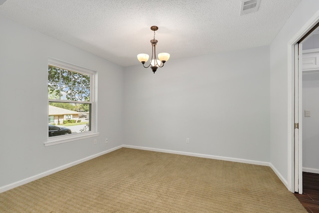 carpeted empty room with a chandelier and a textured ceiling