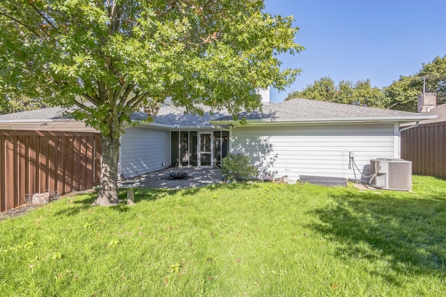 rear view of house with central AC unit and a lawn