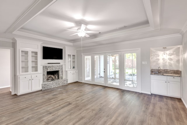 unfurnished living room featuring a raised ceiling, ceiling fan, sink, and wood-type flooring