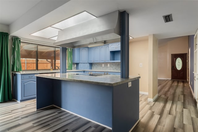 kitchen with light hardwood / wood-style flooring, blue cabinets, backsplash, kitchen peninsula, and black electric stovetop