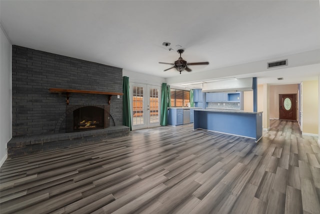 unfurnished living room with ceiling fan, french doors, wood-type flooring, and a brick fireplace