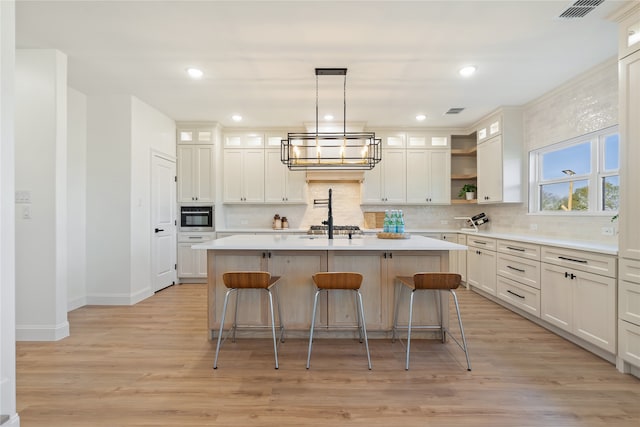 kitchen with stainless steel appliances, light hardwood / wood-style flooring, backsplash, pendant lighting, and a center island with sink