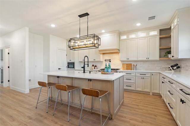 kitchen with light wood-type flooring, a kitchen island with sink, a breakfast bar, sink, and tasteful backsplash