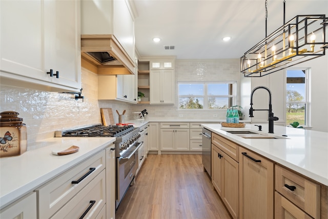 kitchen featuring custom exhaust hood, sink, appliances with stainless steel finishes, decorative light fixtures, and light hardwood / wood-style floors