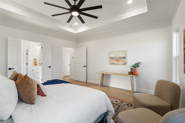 bedroom with a tray ceiling, connected bathroom, ceiling fan, and light hardwood / wood-style floors