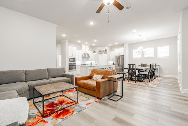 living room featuring ceiling fan with notable chandelier, light hardwood / wood-style floors, and sink