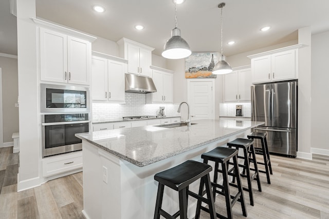 kitchen featuring stainless steel appliances, a kitchen island with sink, sink, decorative light fixtures, and white cabinets