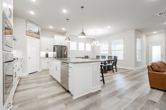 kitchen featuring white cabinetry, an island with sink, pendant lighting, appliances with stainless steel finishes, and light wood-type flooring