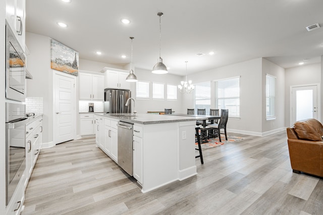 kitchen featuring white cabinetry, an island with sink, pendant lighting, appliances with stainless steel finishes, and light wood-type flooring