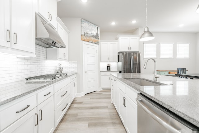 kitchen featuring white cabinets, sink, appliances with stainless steel finishes, decorative light fixtures, and light hardwood / wood-style floors