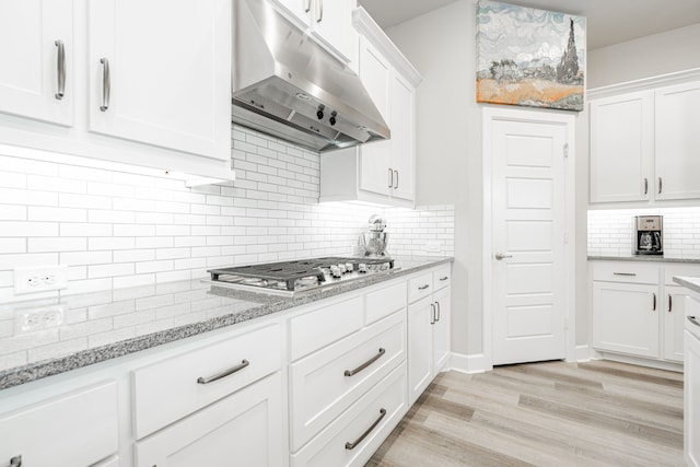 kitchen with light stone countertops, stainless steel gas cooktop, backsplash, light hardwood / wood-style floors, and white cabinets