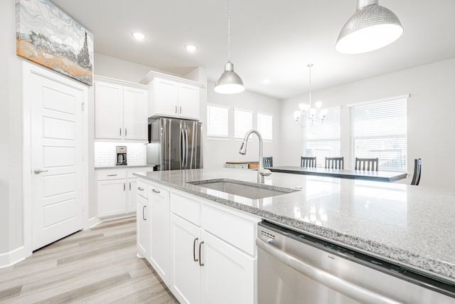 kitchen featuring sink, light stone countertops, appliances with stainless steel finishes, light hardwood / wood-style floors, and white cabinetry