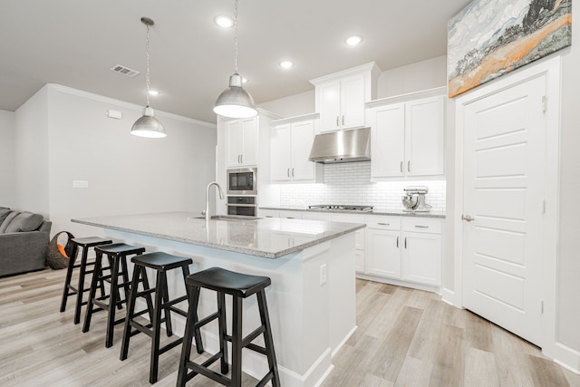 kitchen featuring white cabinetry, light stone countertops, light hardwood / wood-style flooring, an island with sink, and appliances with stainless steel finishes