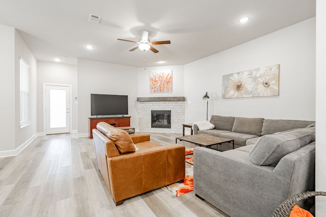 living room with light hardwood / wood-style floors, a brick fireplace, and ceiling fan