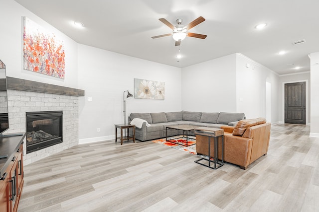 living room featuring ceiling fan, light hardwood / wood-style floors, ornamental molding, and a fireplace