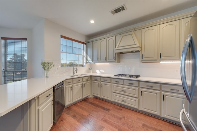 kitchen featuring sink, stainless steel appliances, premium range hood, kitchen peninsula, and hardwood / wood-style flooring