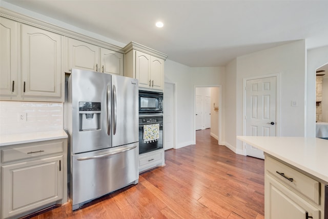 kitchen featuring decorative backsplash, cream cabinetry, black appliances, and light hardwood / wood-style floors