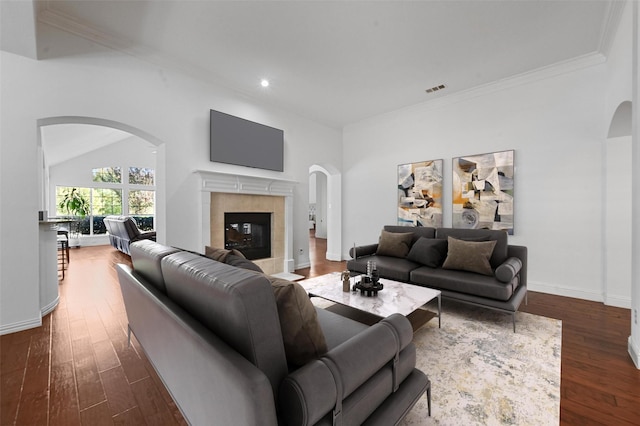 living room with dark wood-type flooring, vaulted ceiling, crown molding, and a tiled fireplace