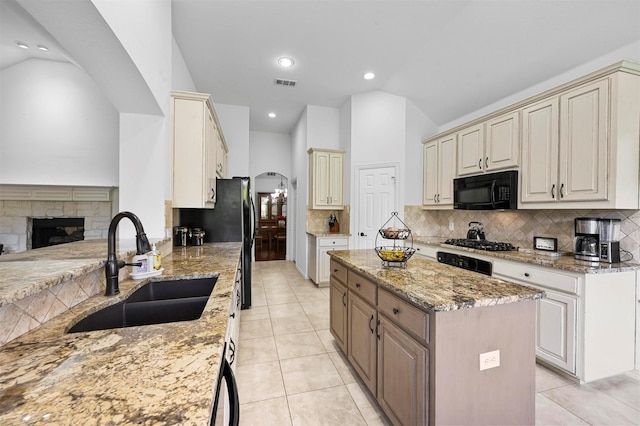 kitchen featuring light stone counters, black appliances, decorative backsplash, a fireplace, and sink