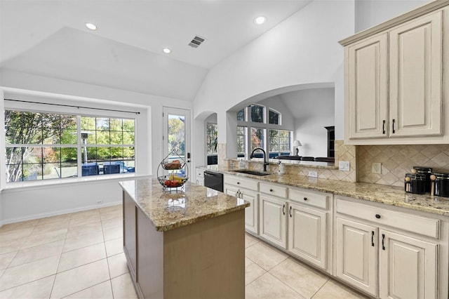 kitchen featuring light stone countertops, lofted ceiling, decorative backsplash, sink, and light tile patterned flooring