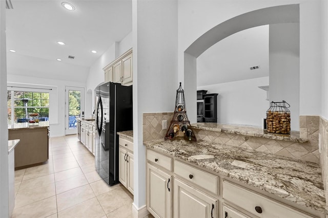 kitchen with light tile patterned floors, light stone countertops, cream cabinets, and black refrigerator