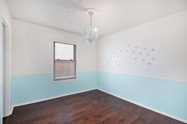 spare room featuring dark wood-type flooring and a chandelier